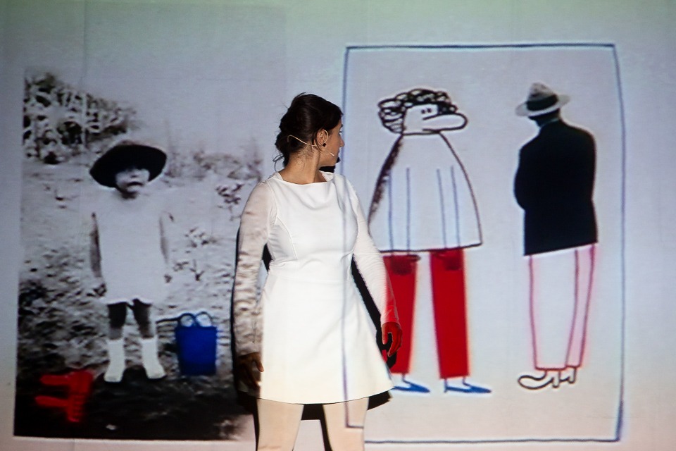 Madalena Marques olha por cima do ombro para os desenhos de um homem e uma mulher desenhados e projetados por Catarina Sobral, durante o espetáculo «Impossível». 