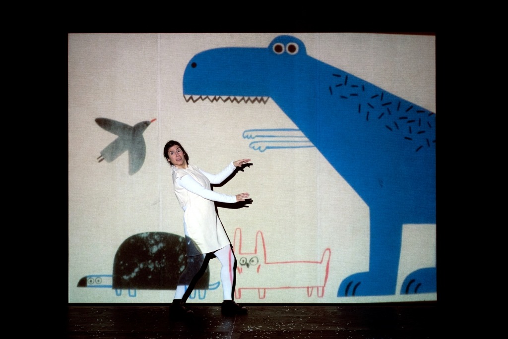A atriz Madalena Marques interage com o desenho projetado de um dinossáurio.