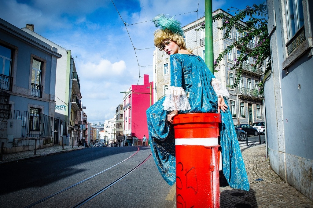 Com um vestido do século XVIII, a  atriz Crista Alfaiate está sentada num marco do correio. 