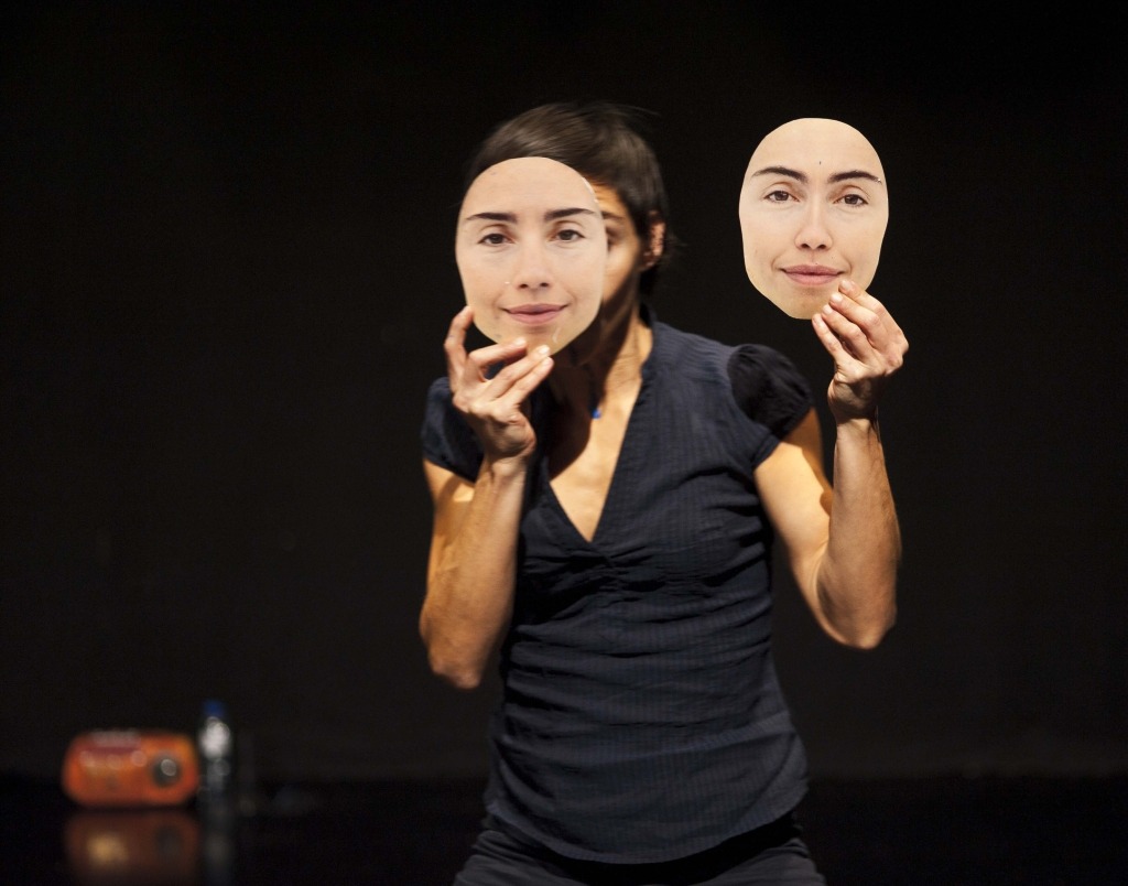 Pessoa cobre o rosto com duas máscaras nas quais estão impressas dois rostos.
