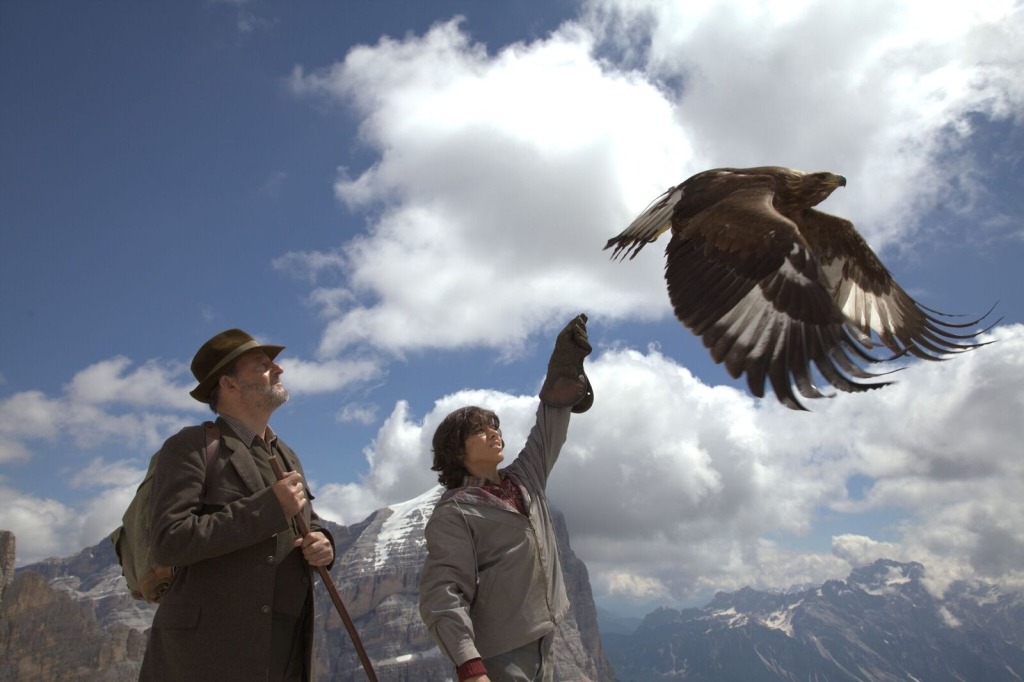 Um homem e uma criança olham para uma águia em pleno voo.