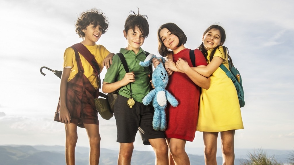 Quatro crianças de frente para o observador vestidas com cores coloridas.
