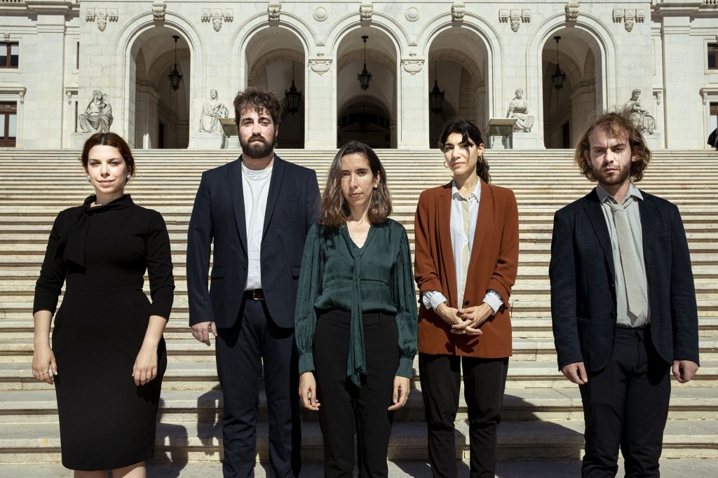 Cinco pessoas vestidas de modo formal posam à frente das escadarias da Assembleia da República portuguesa.