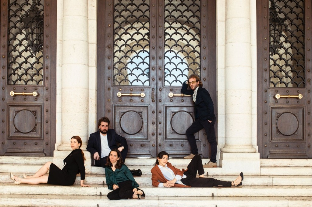 Cinco pessoas, vestidas de modo formal, nas escadarias de um edifício imponente.