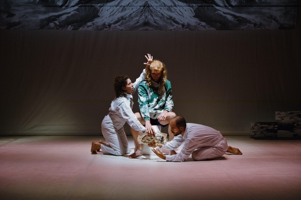 Três bailarinos juntos no centro de um palco mal iluminado
