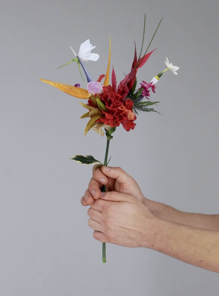Duas mãos seguram um arranjo floral com um cravo vermelho ao centro