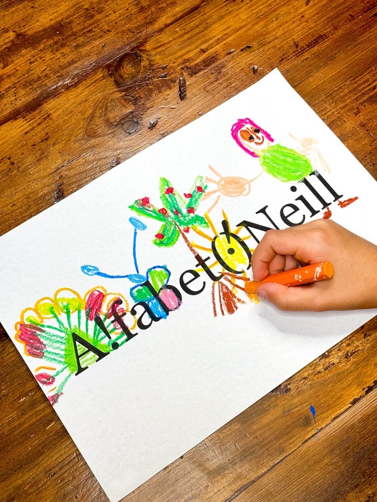 Hand paints with crayons on a white sheet of paper with AlphabetO