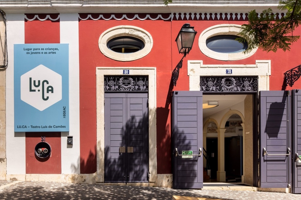 Parte da fachada do teatro LUCA de cor vermelha escura e portas azuis escuras